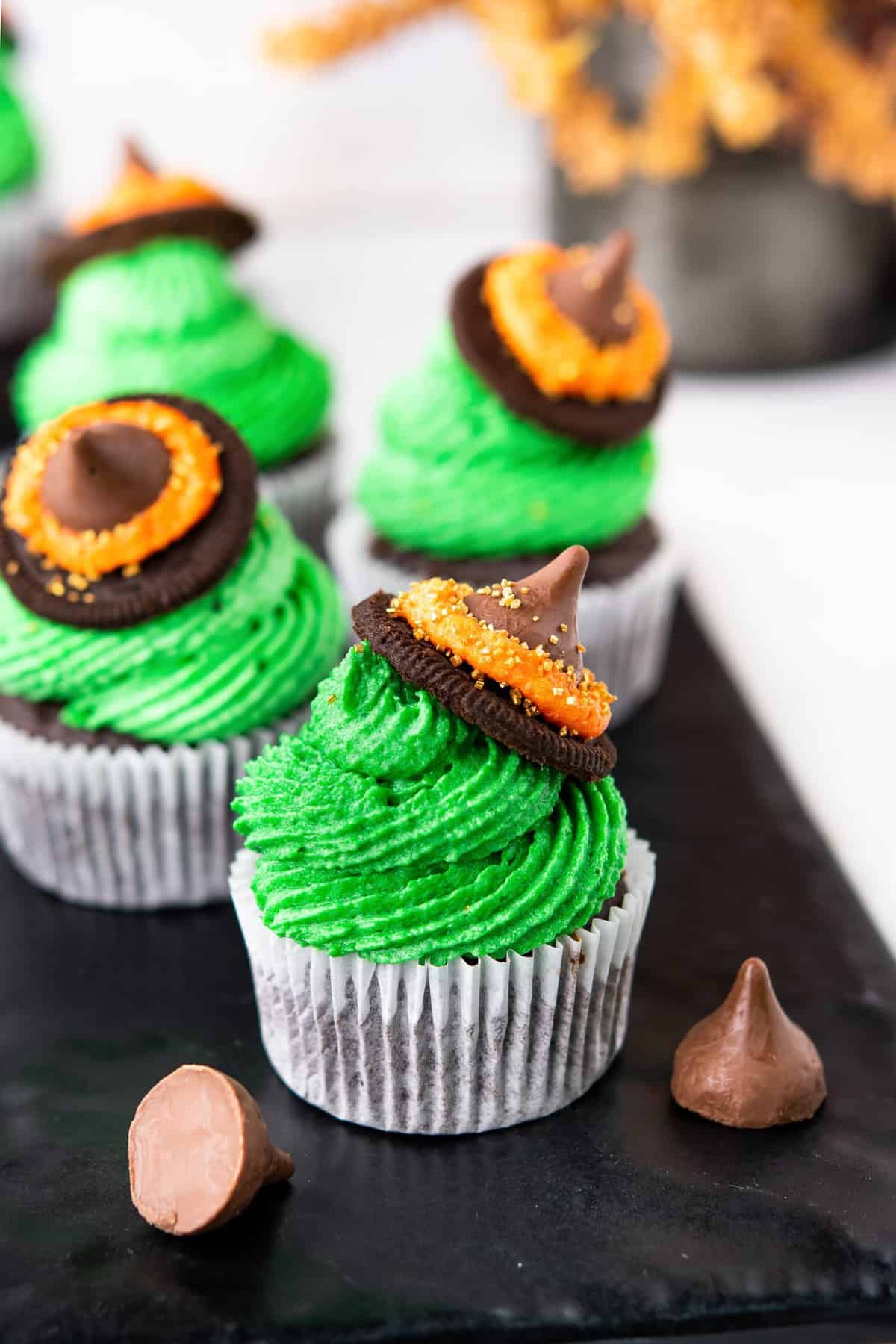 Cupcakes with green frosting and an oreo and hershey kiss witch hat on top. 