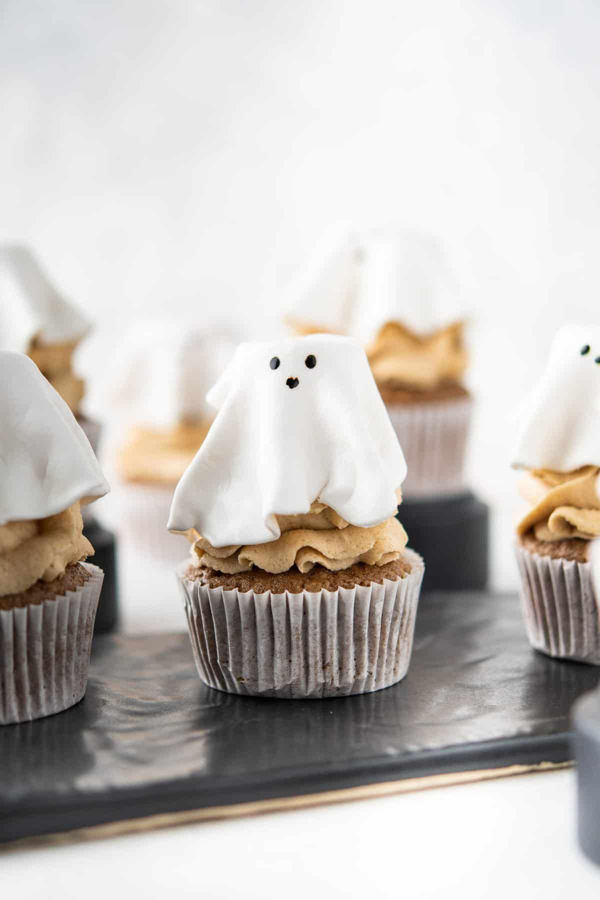 Ghost topped cupcakes with coffee frosting on a black rectangle dish. 