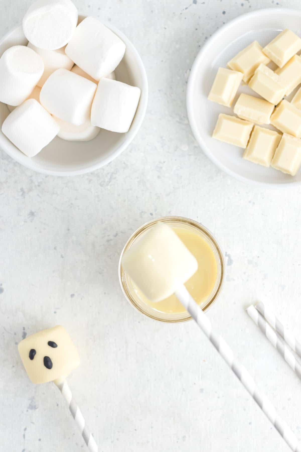 Dipping the marshmallow stick into white chocolate. Bowl of marshmallows and chocolate on the side. 