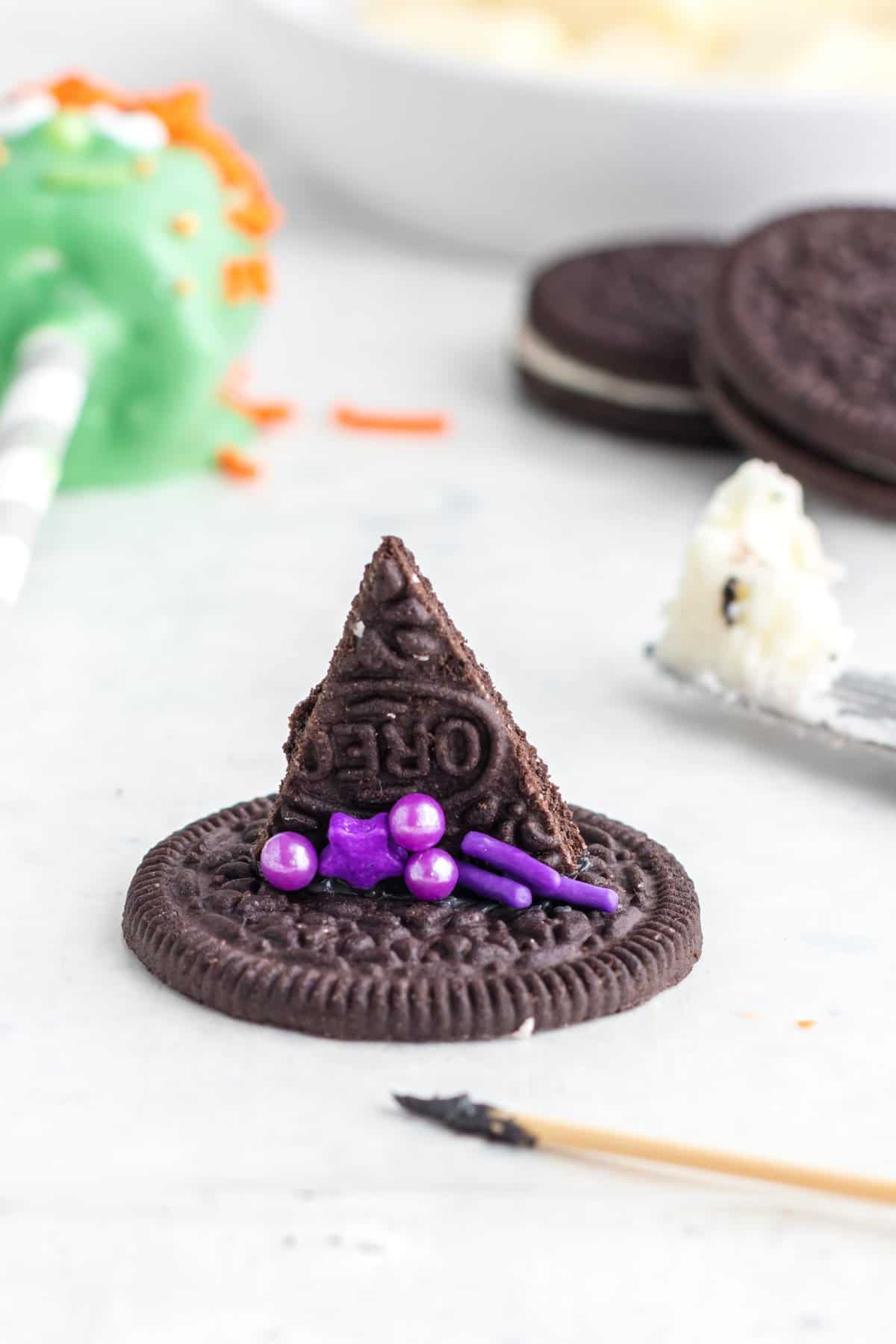 decorating the oreo witch hat with purple sprinkles. 