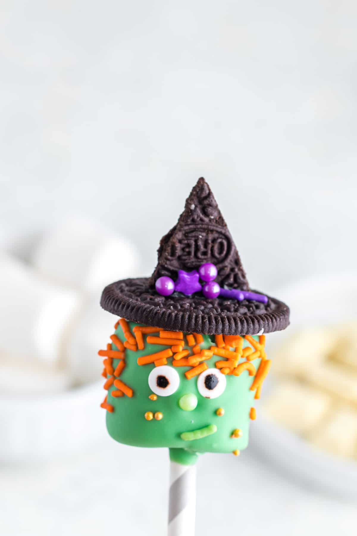 Placing the hat and orange sprinkles onto the green marshmallow, creating the witch. 