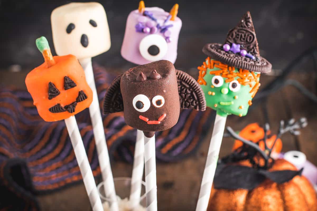 Shot of the five different marshmallow pops with pumpkin in the background. 