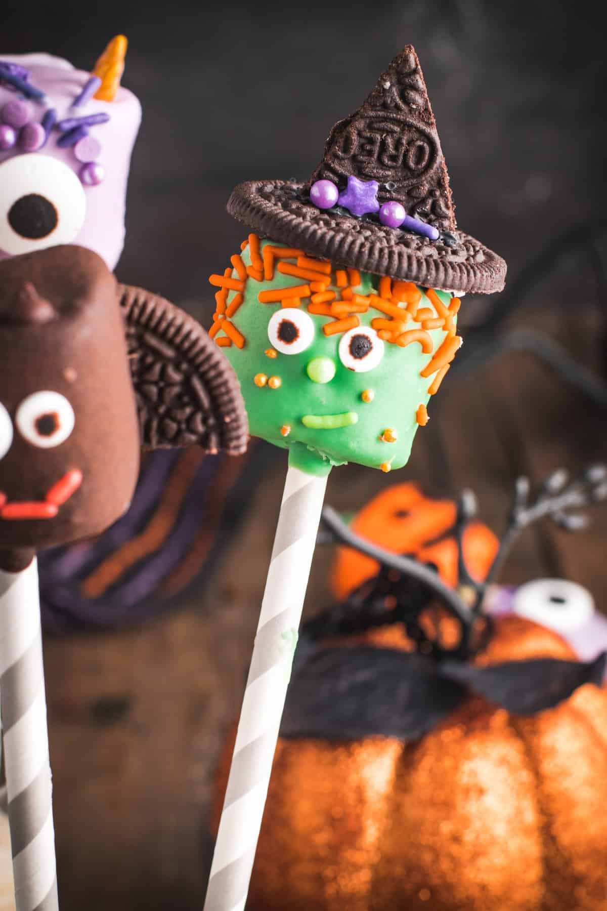 Cute witch marshmallow pop on a paper straw with pumpkin in background. 