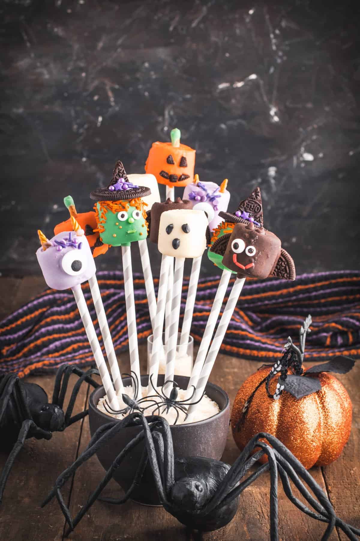 dipped marshmallow halloween treats on purple and white straws standing up in a black cauldron. 