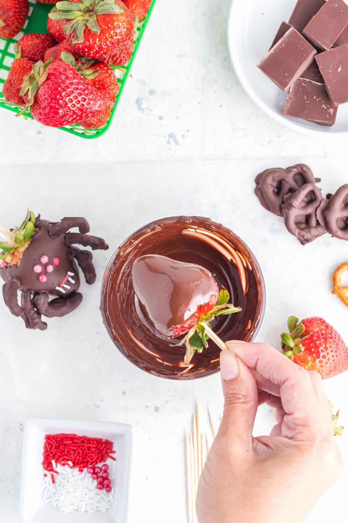 Hand dipping the strawberry into the bowl of melted chocolate. 