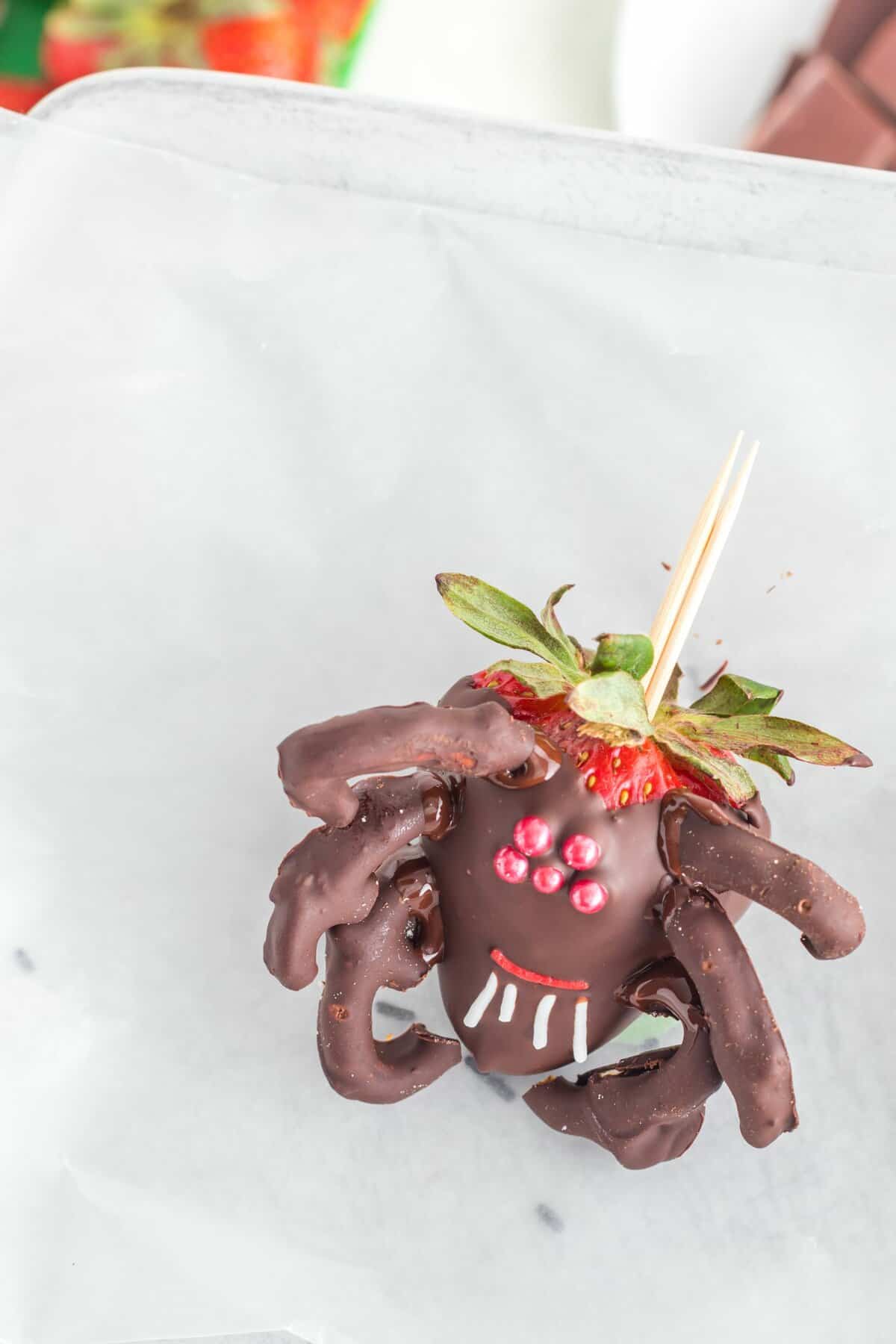 The finished black widow decorated chocolate dipped strawberry on piece of wax paper.