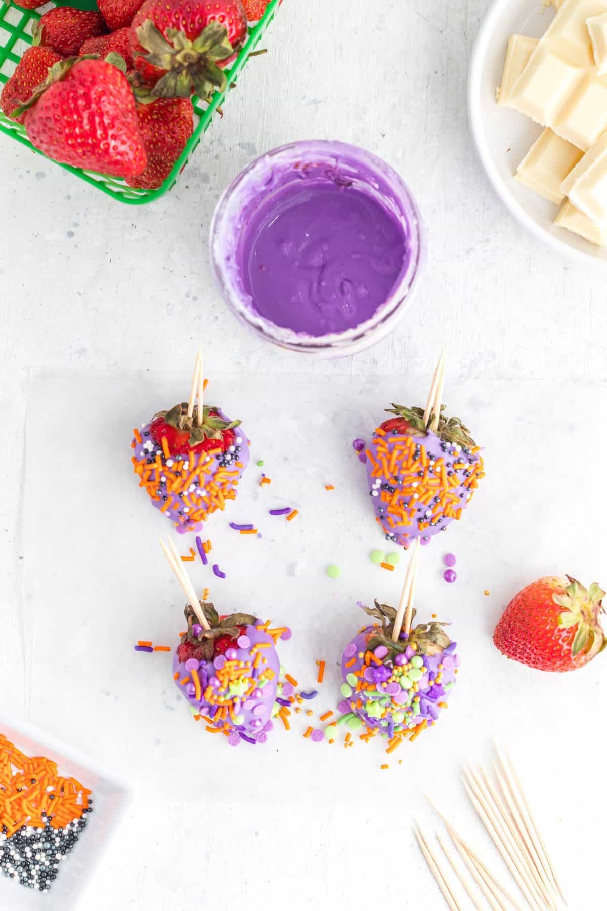Bowl of purple melted chocolate and dipped strawberries with halloween sprinkles. 