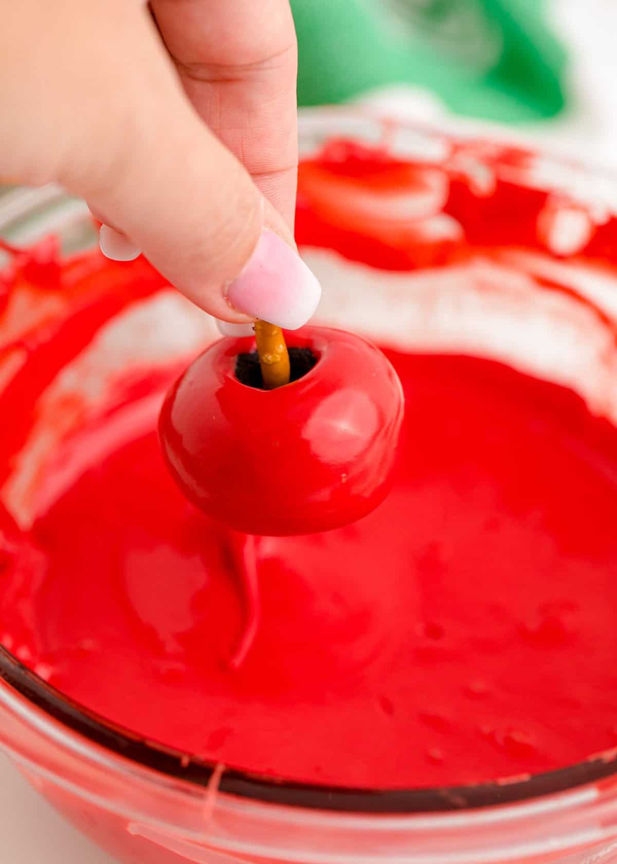 Hand pulling the oreo ball out of the melted red chocolate and letting it drip. 