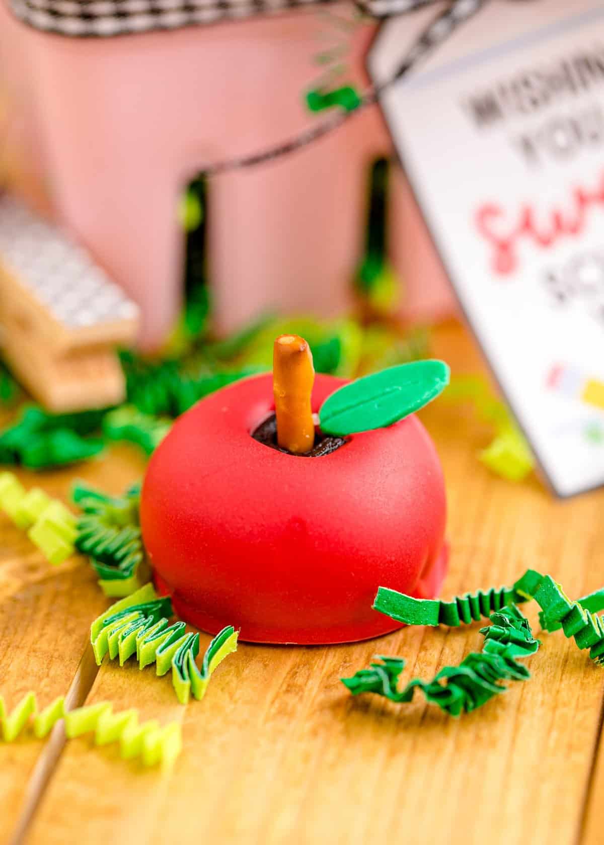An individual red apple shaped oreo ball with pretzel stem and fondant leaf. 
