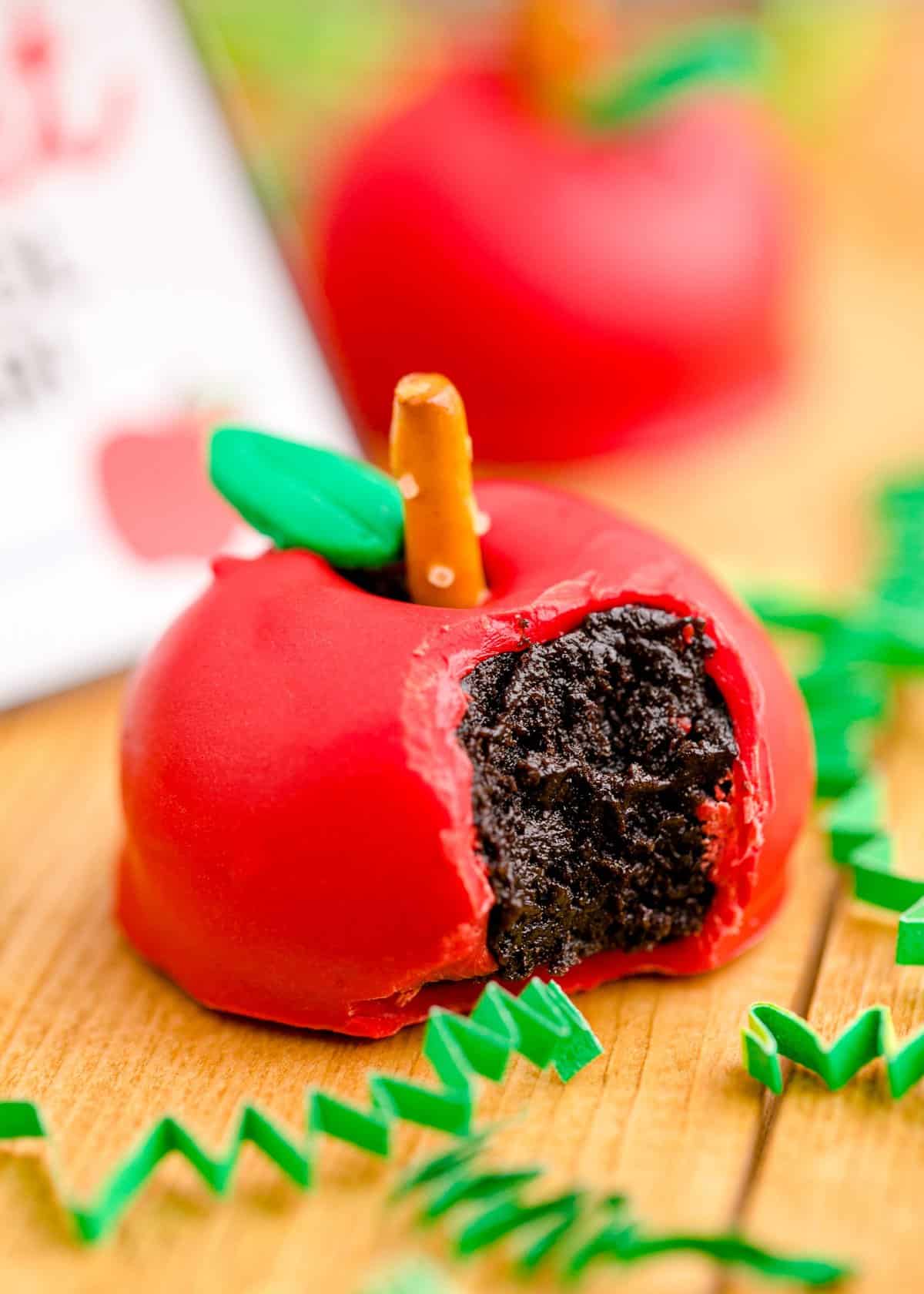 An apple oreo ball on a wood counter with a bite taken out exposing the oreo truffle center.