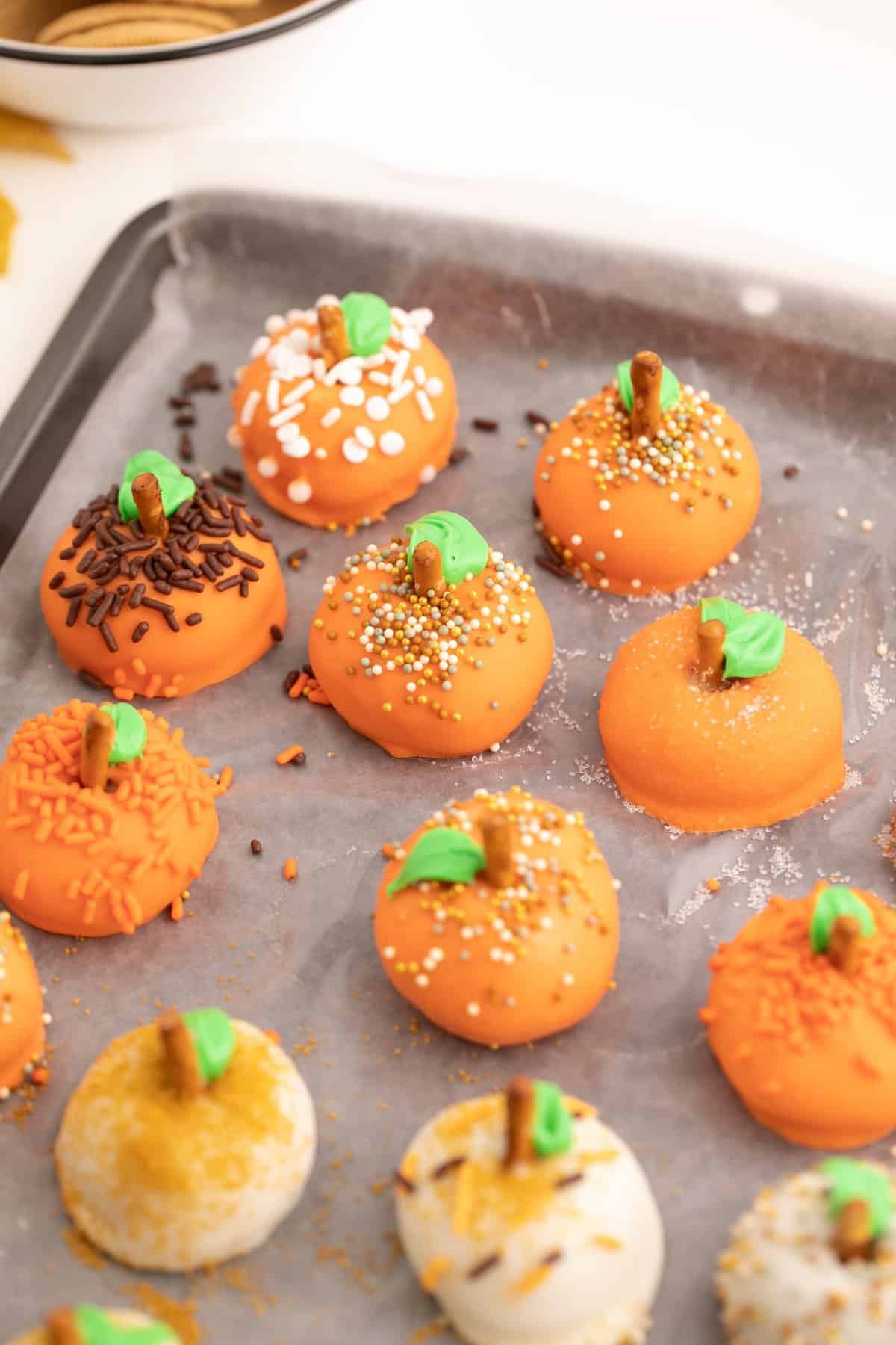 Orange and white oreo truffles with the green leaves and sprinkles on cookie sheet. 