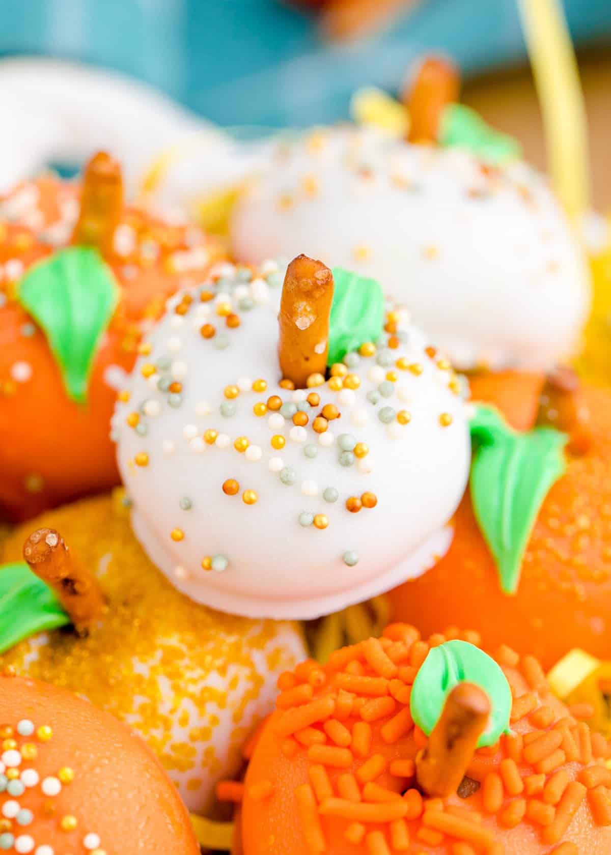 Up close shot of a white pumpkin truffle with pretzel stem and gold sprinkles. 