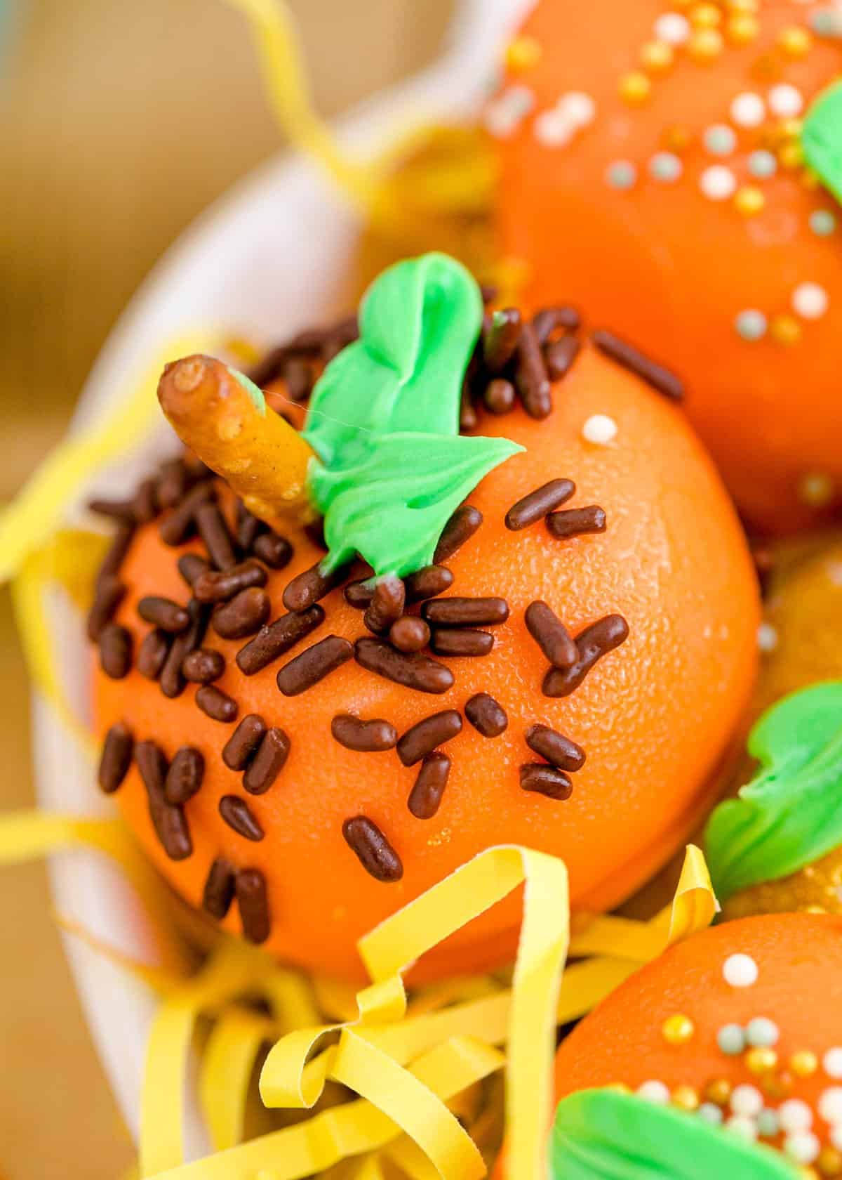 Up close shot of an orange pumpkin with mini chocolate sprinkles and a pretzel stem. 