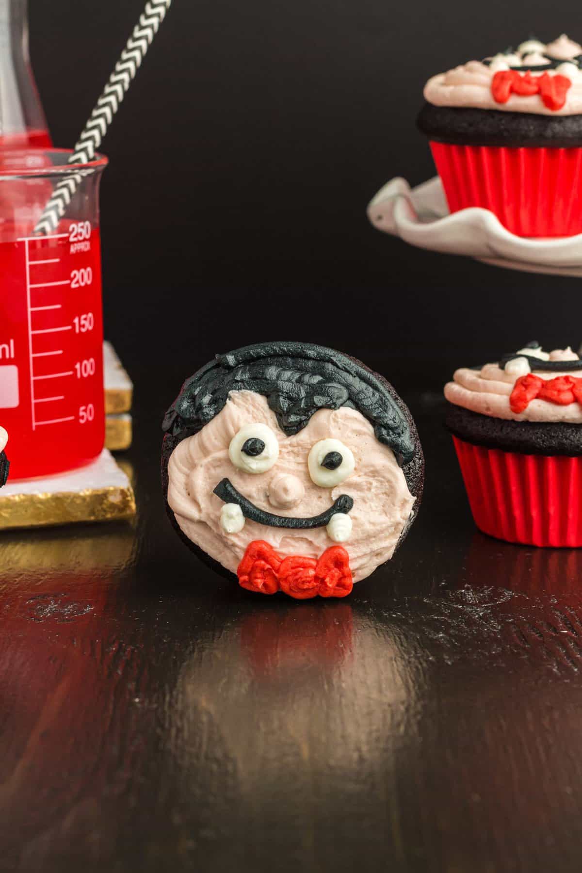 Cupcake on its side to show vampire face with white cake plate in the background.