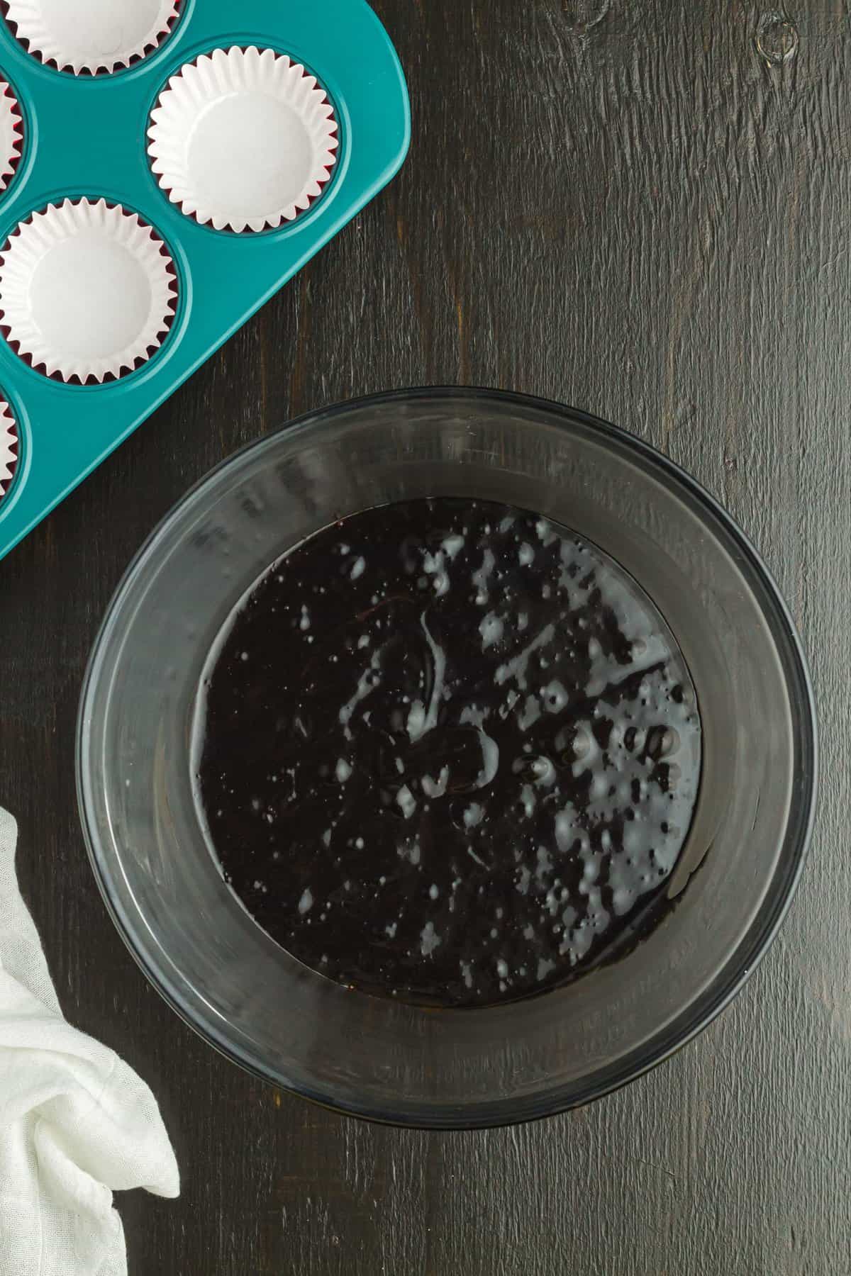 Adding black food coloring to the chocolate cupcake batter in glass bowl. 
