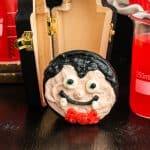 Square image of a vampire face cupcake with a wood coffin in background.