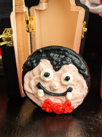 Square image of a vampire face cupcake with a wood coffin in background.
