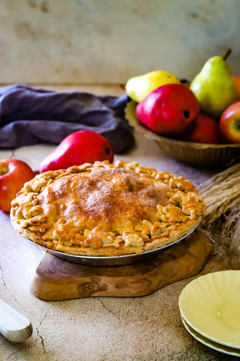 Apple pear pie on a wood piece with bowl of apples and pears in background. 