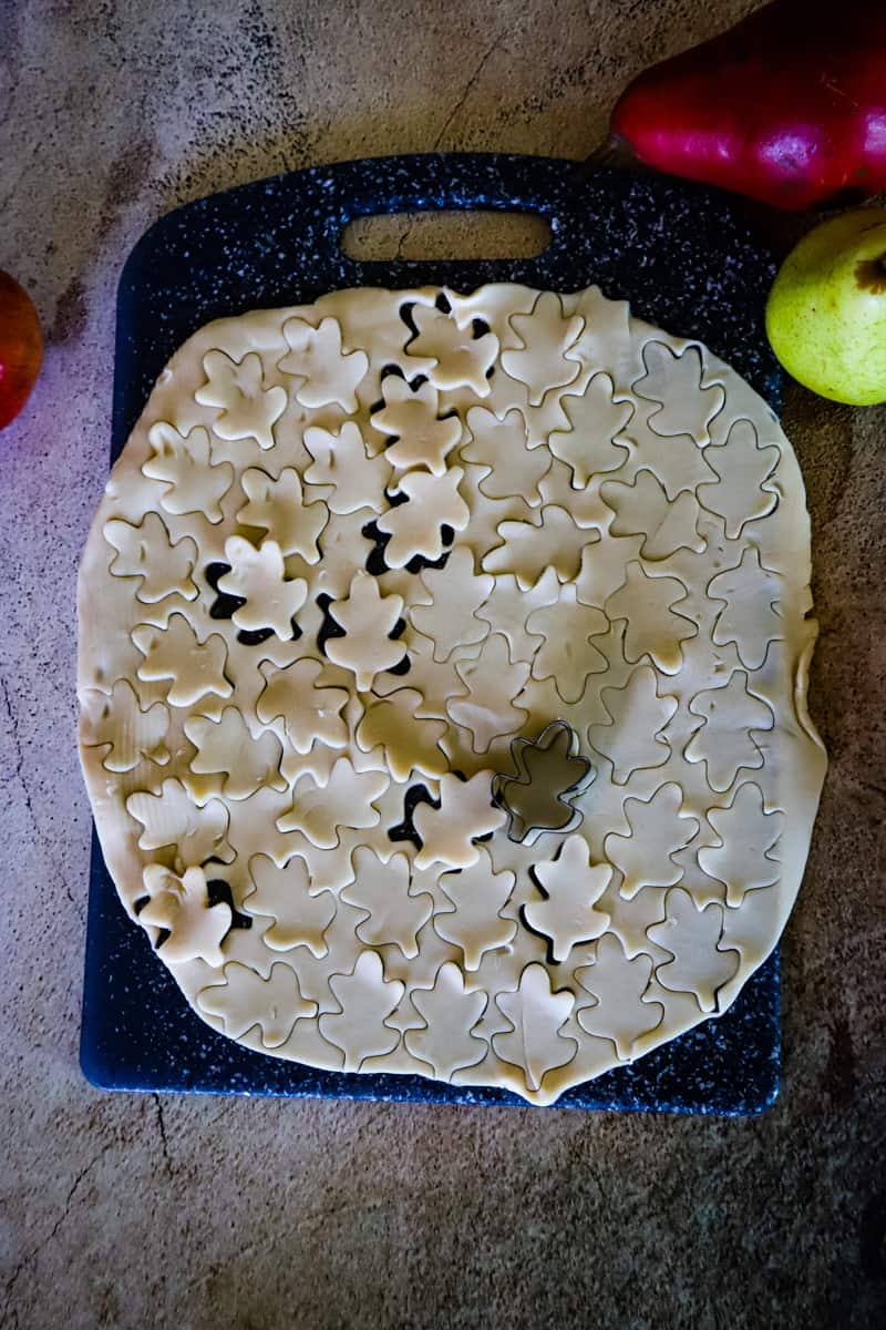 rolled pie crust with a leaf cookie cutter cutting out mini leaves. 