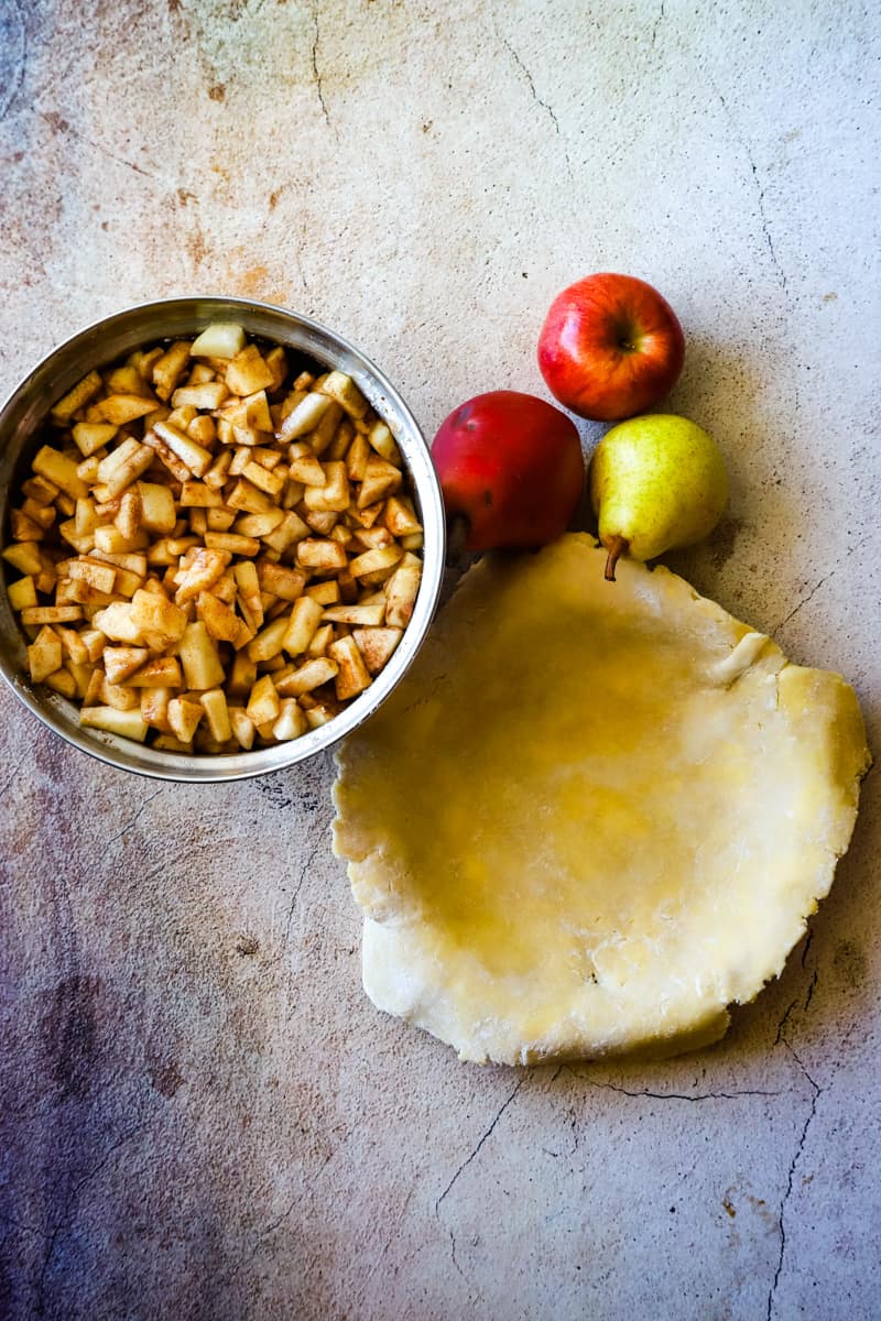 Overhead shot of a bowl with the apple pear pie filling and a pie tin lined with bottom crust.