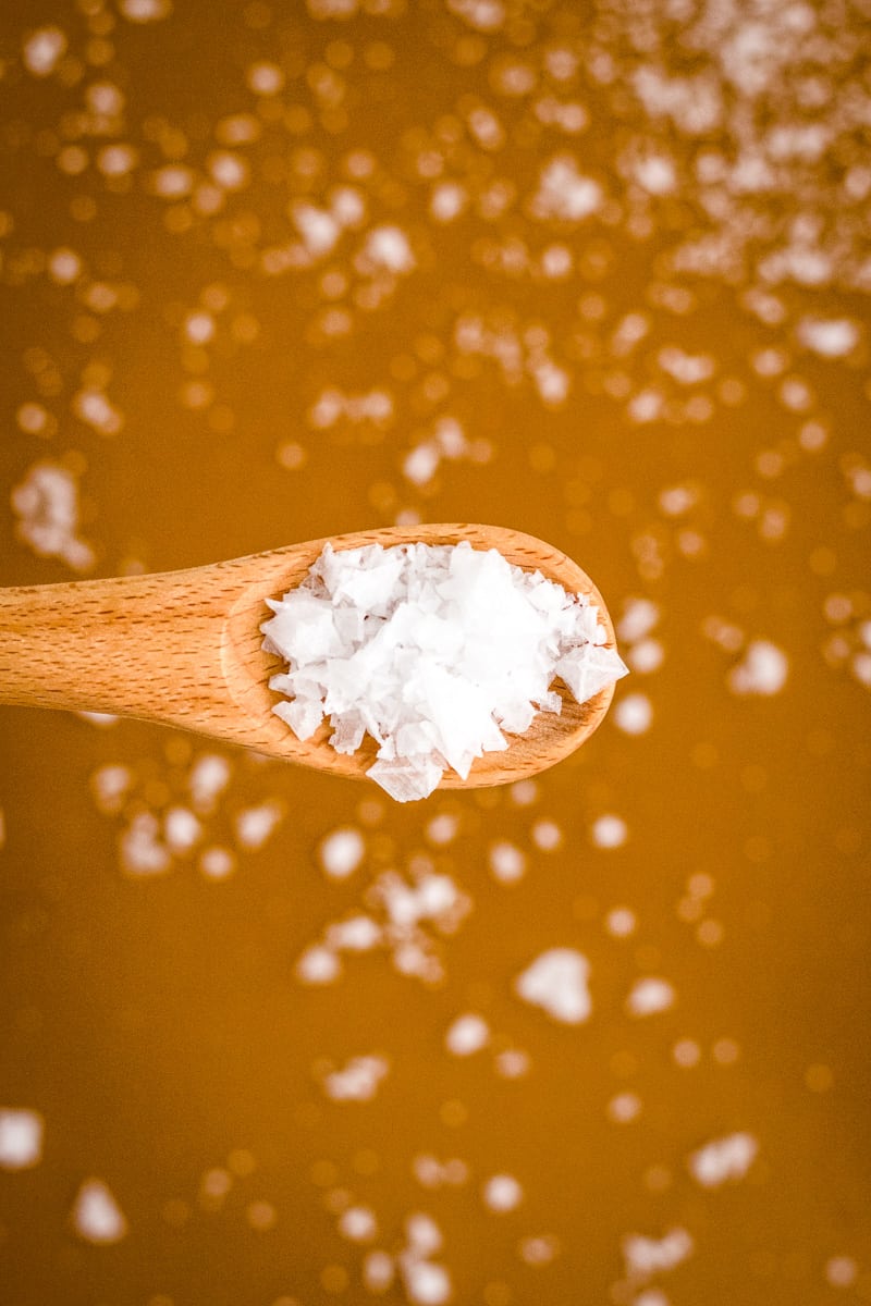 Wooden spoon above the pan of caramel sprinkling the flaked sea salt. 