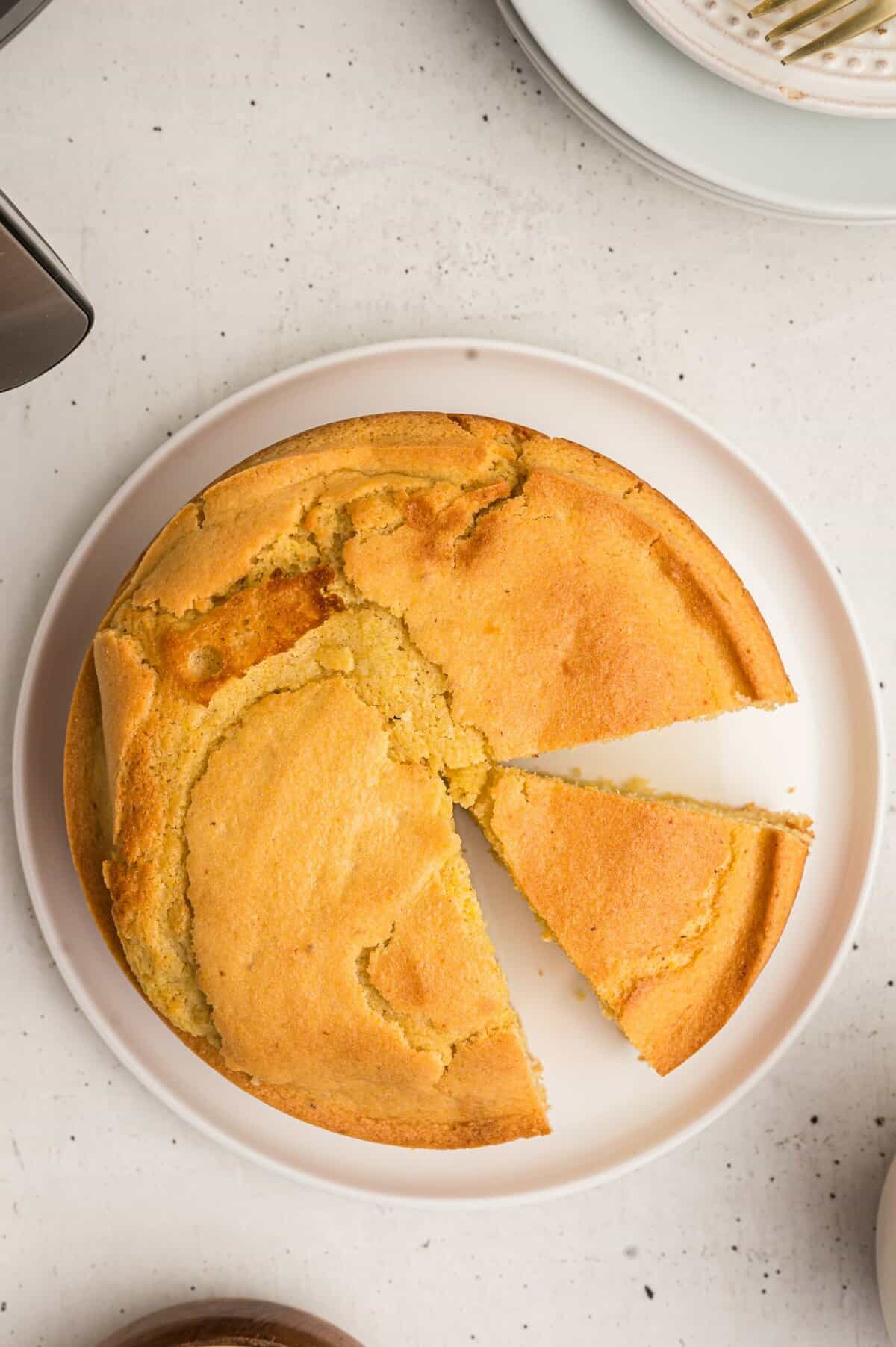 Overhead shot of the round cornbread with a slice removed on white plate. 