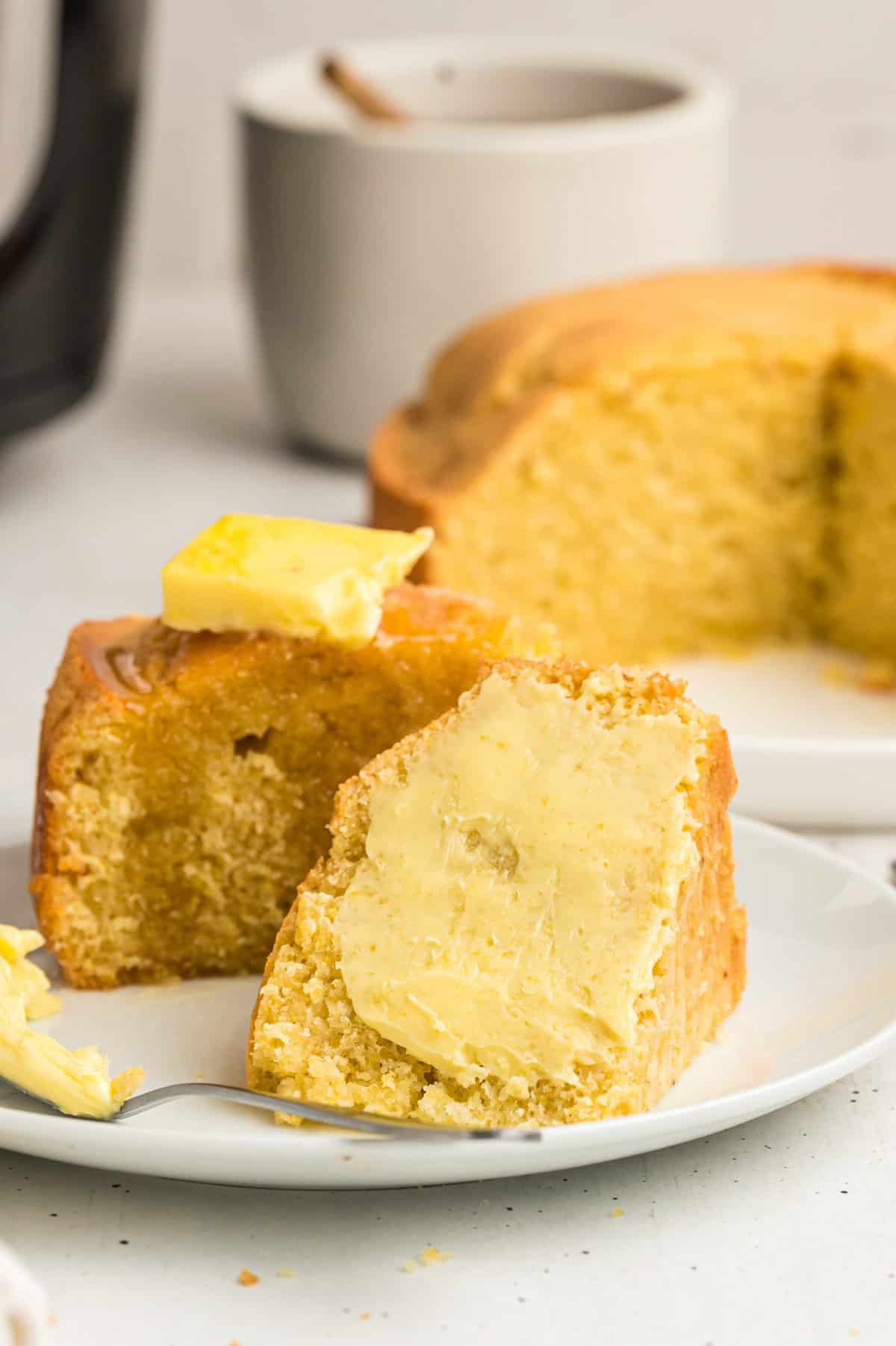 Two slices of cornbread spread with butter on small white plate. 