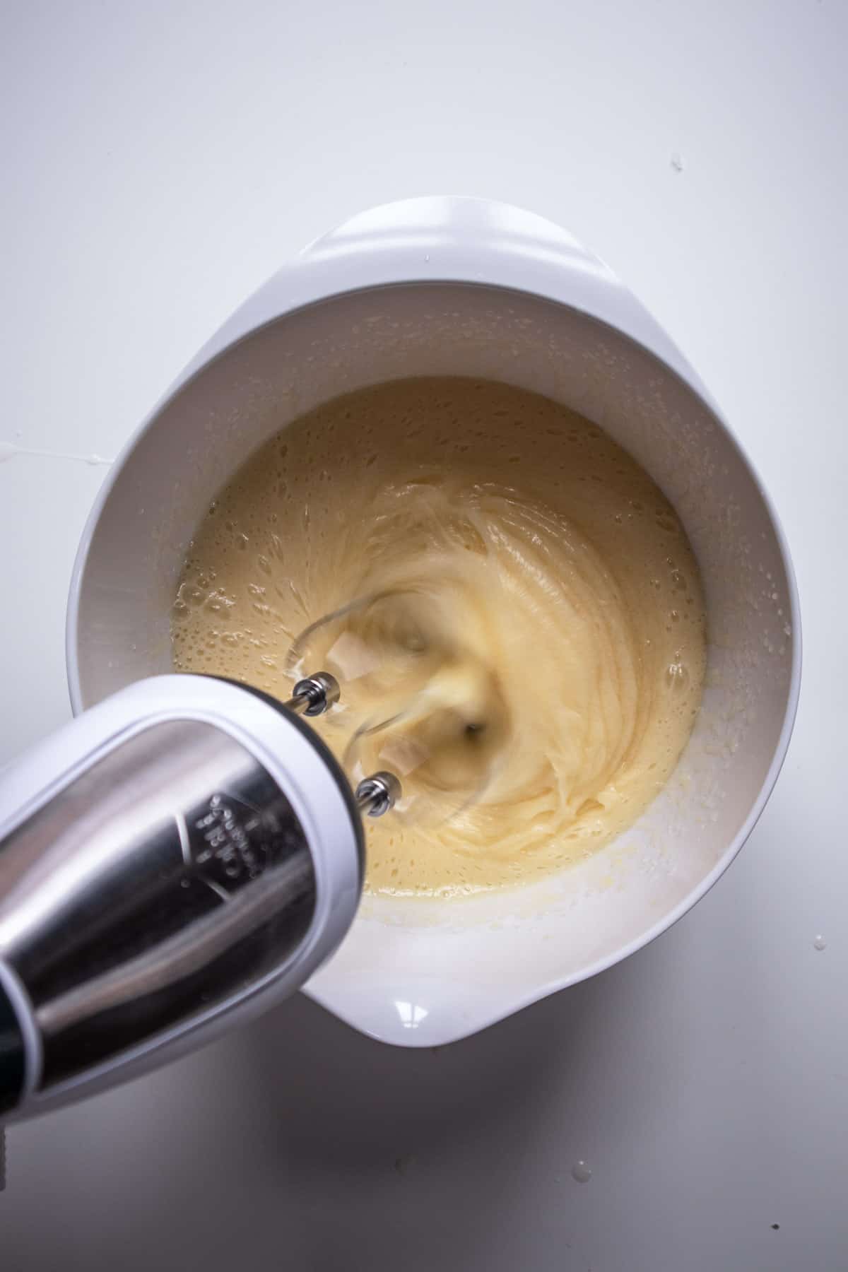 Hand mixer beating the pumpkin cupcake batter in large white bowl. 