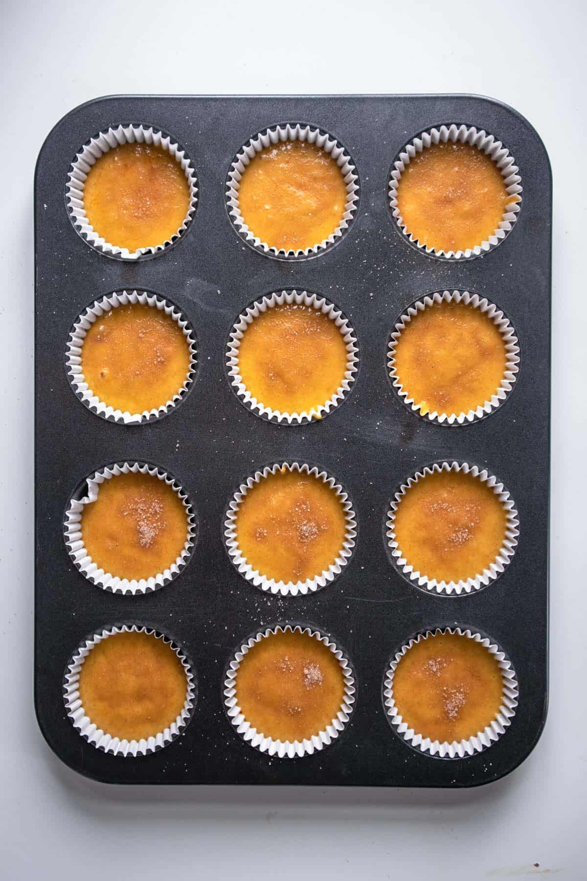 A cupcake pan filling with liners and pumpkin cupcake batter. 