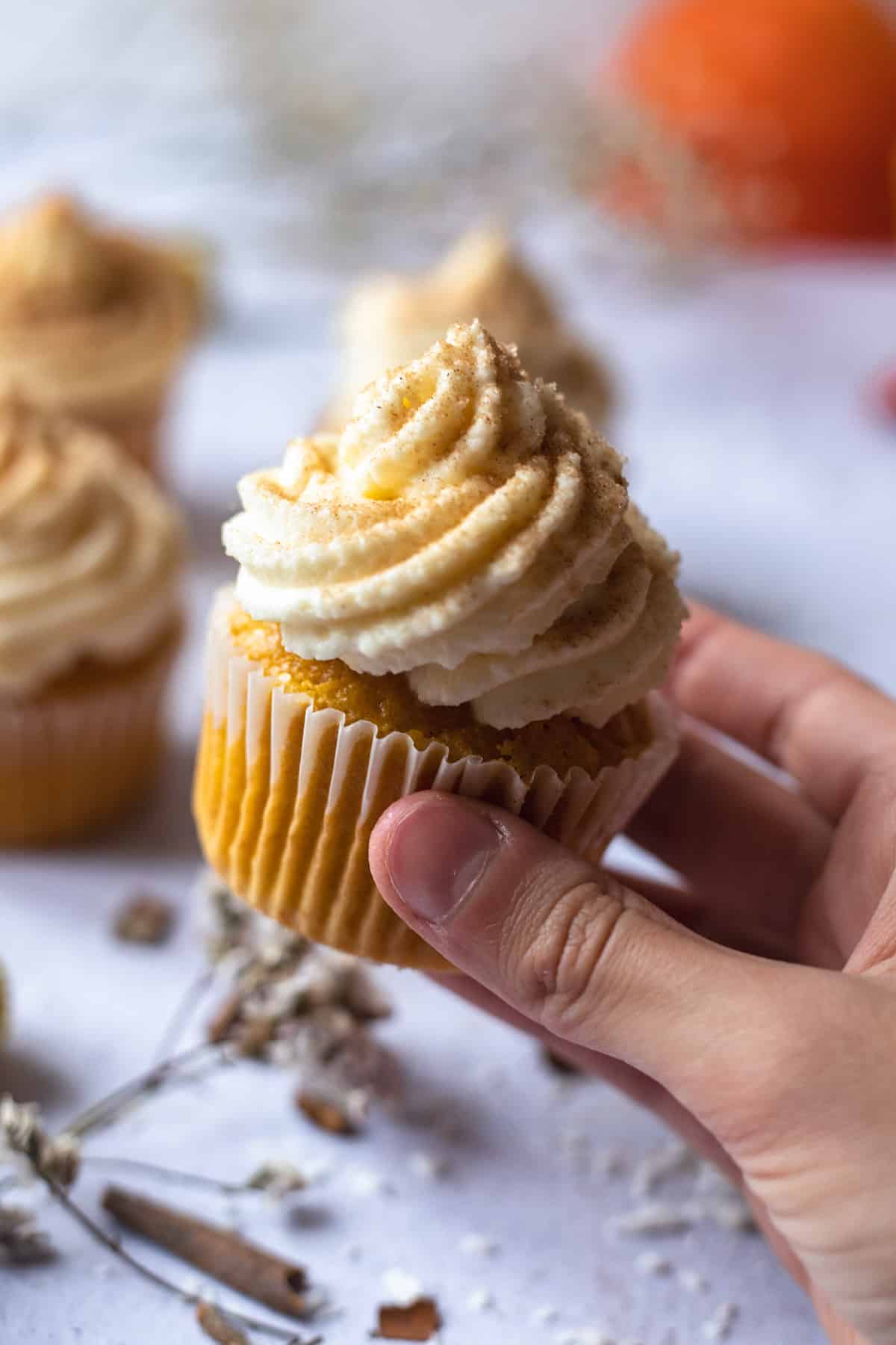 Hand holding up the frosting cupcake sprinkled with cinnamon and sugar. 