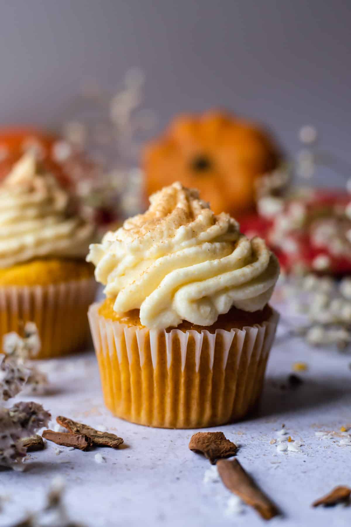 Shot of a single cupcake on white table with orange pumpkin in the background.