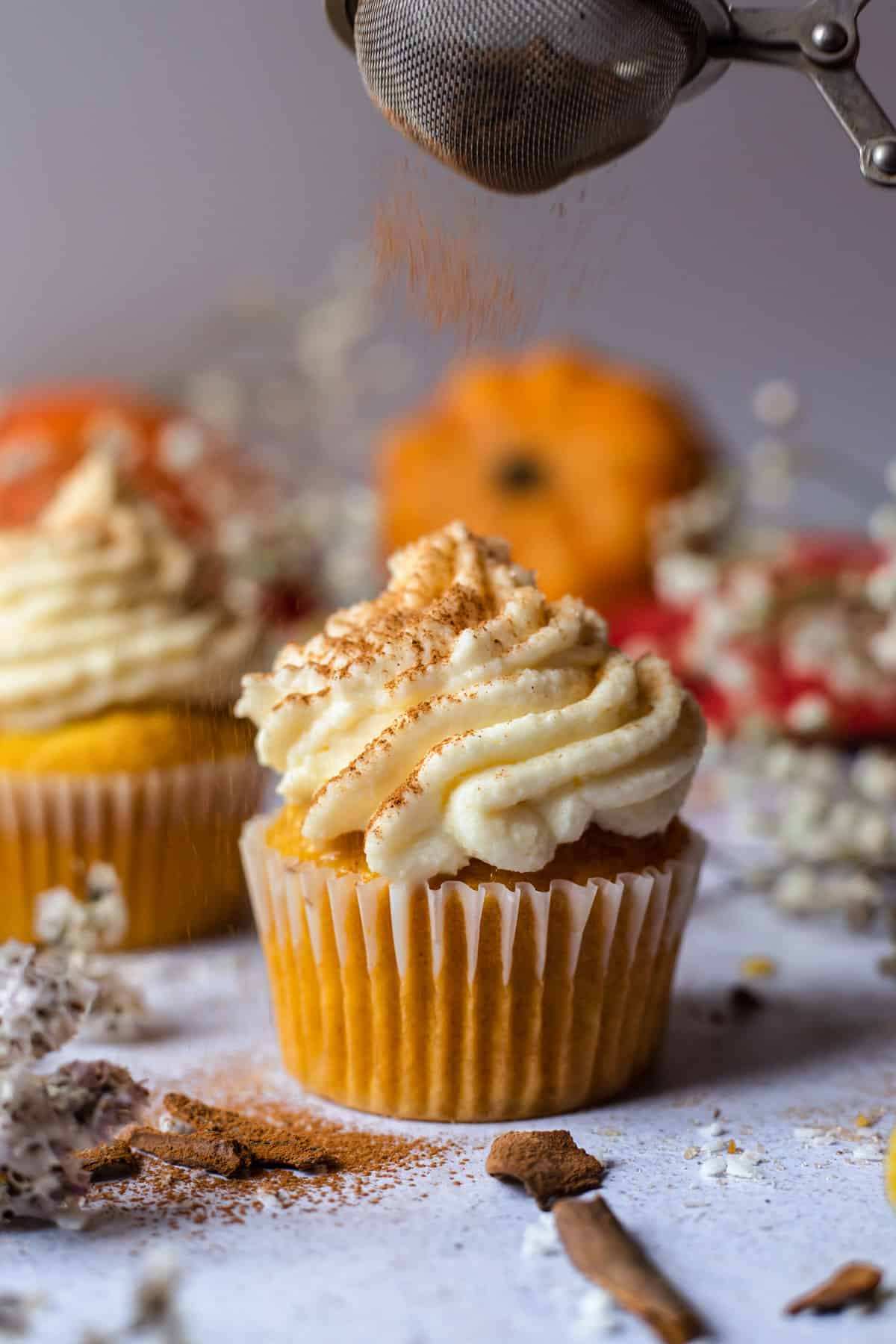 Cupcake being sprinkled with ground cinnamon on decorated white surface. 