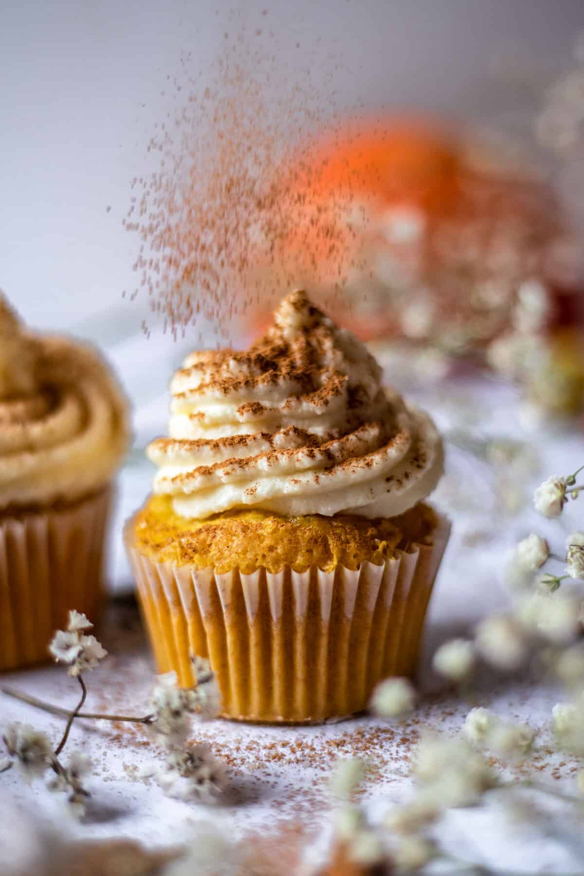 pumpkin cupcake with frosting being sprinkled with ground cinnamon. 
