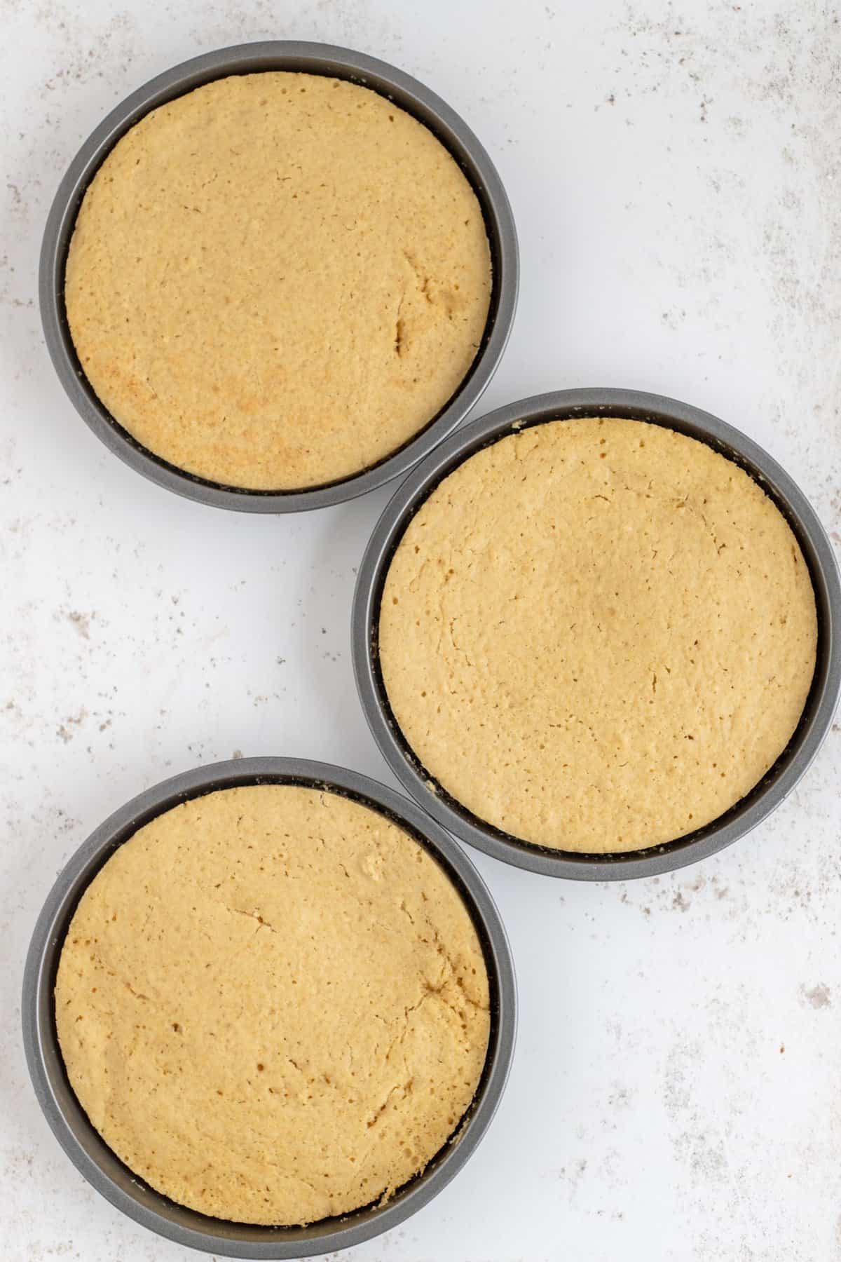 Three cooked maple cake layers in round pans on white background. 