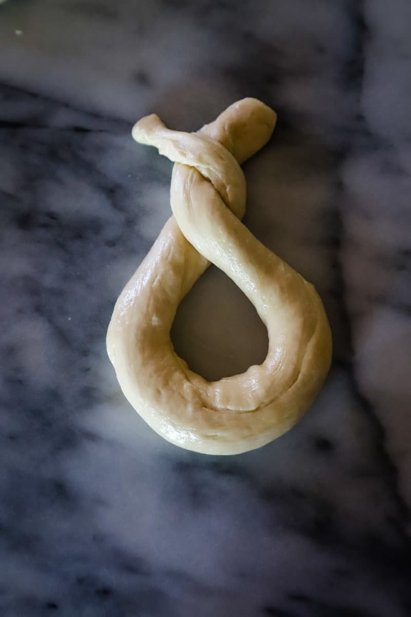 Twisting the edges of the dough rope together to form a pretzel. 