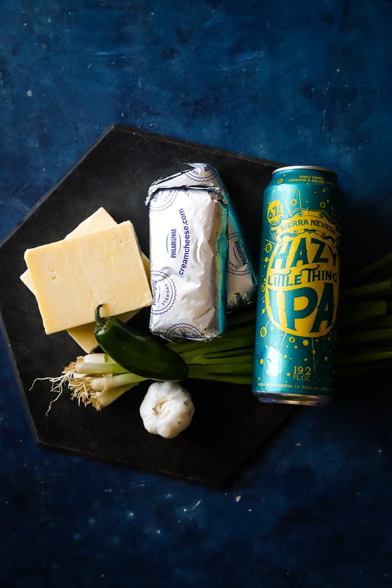 Overhead shot of the beer cheese ingredients on black cutting board and blue surface. 