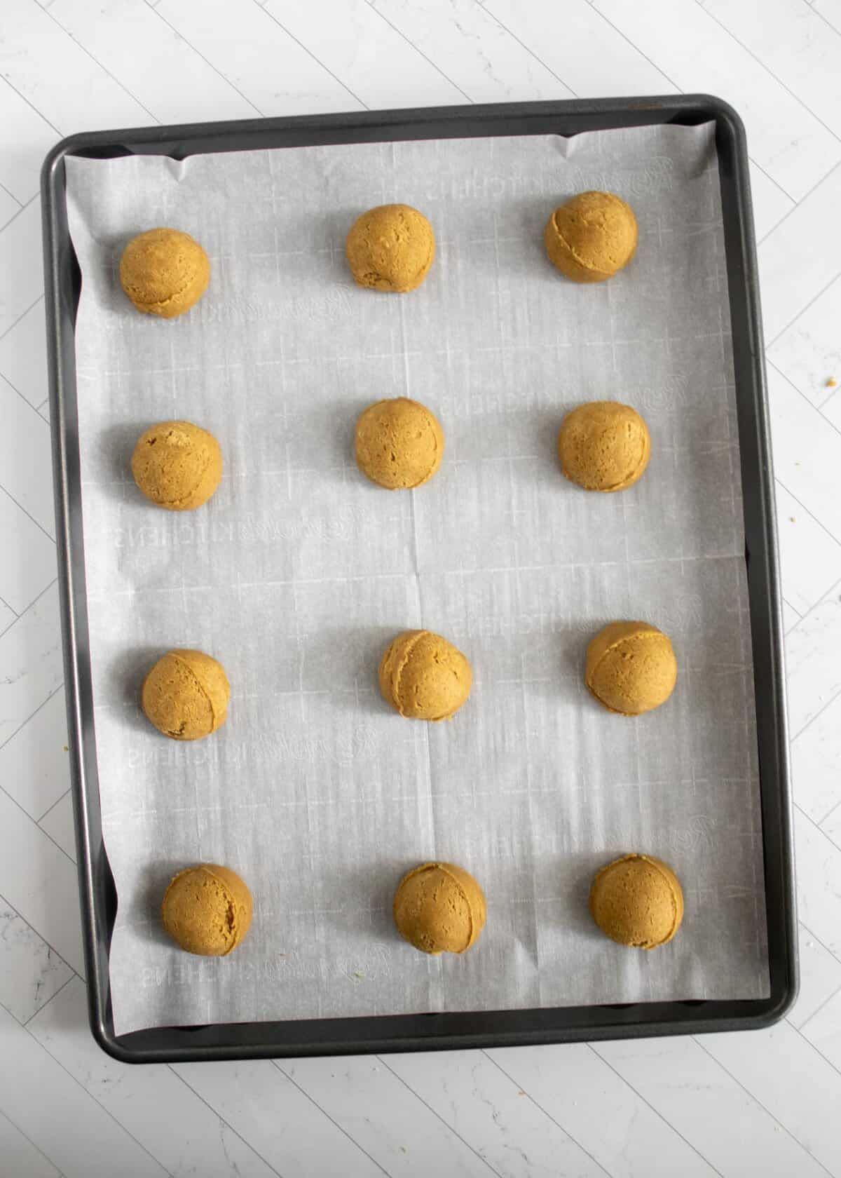 rolled gingerbread balls on a parchment lined cookie sheet. 