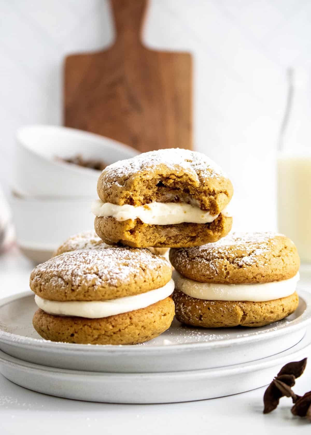 Three gingerbread cookie sandwiches stacked on white plate with top cookie having a bit taken out of it. 