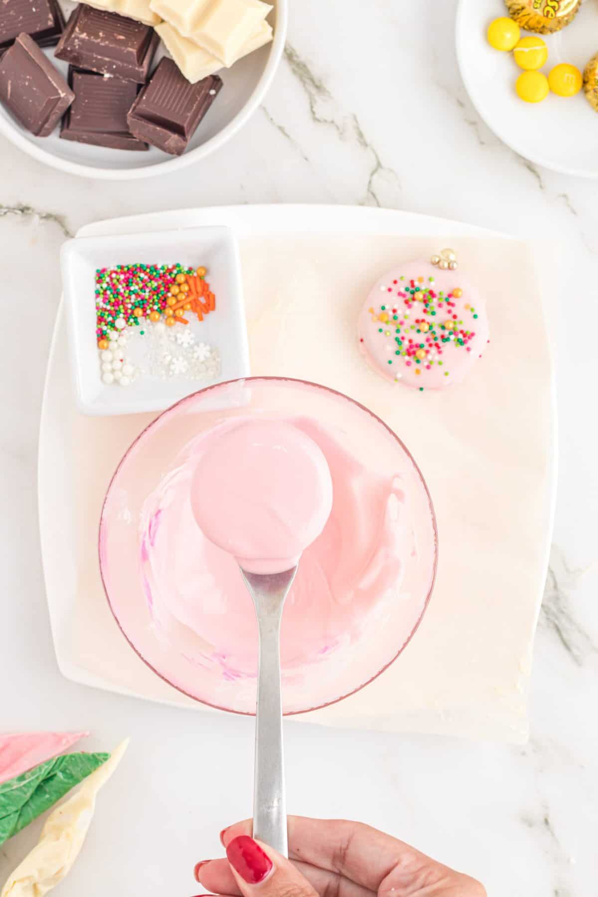 Fork dipping oreo in a bowl of pink white chocolate 