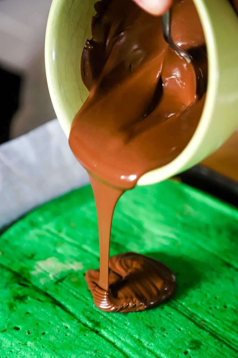 Hand pouring green bowl of melted chocolate over chilled bars. 