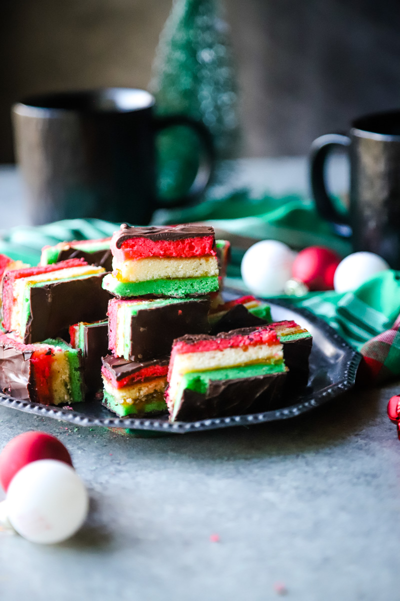 red, white, and green layered cookies on a silver plate with coffee cup in background. 