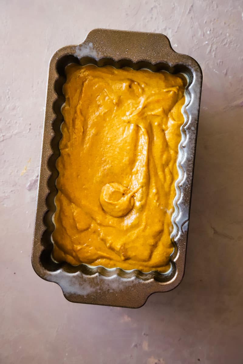 Pouring the pumpkin loaf batter into the metal loaf pan. 