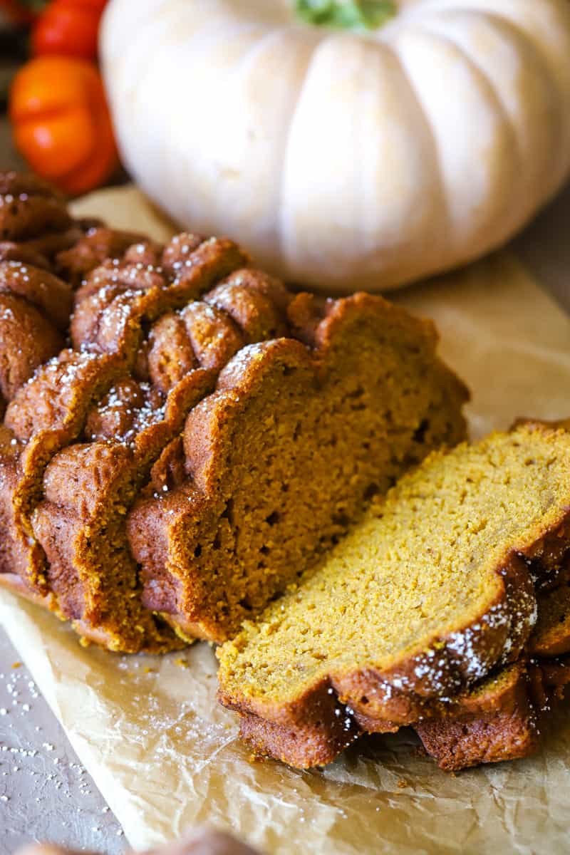 Pumpkin loaf cut into slices with white pumpkin in the background. 