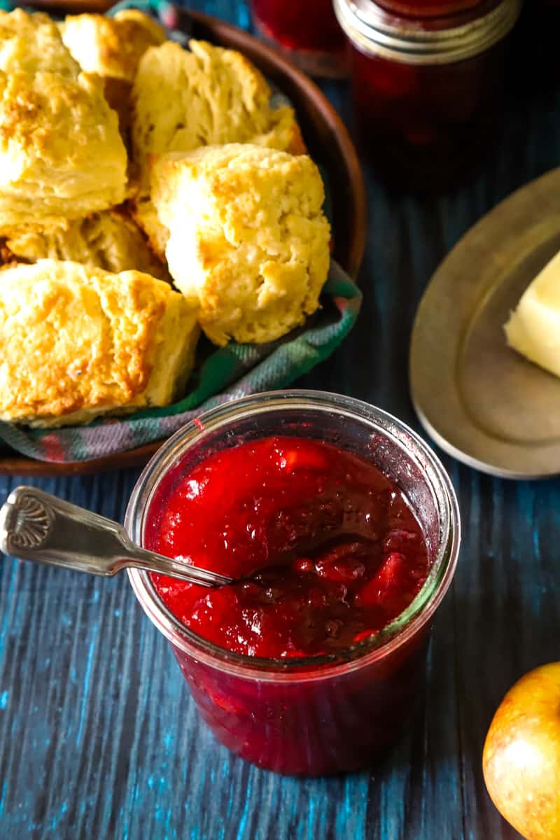 Large weck jar with cranberry apple jam and a bowl of biscuits in the corner. 