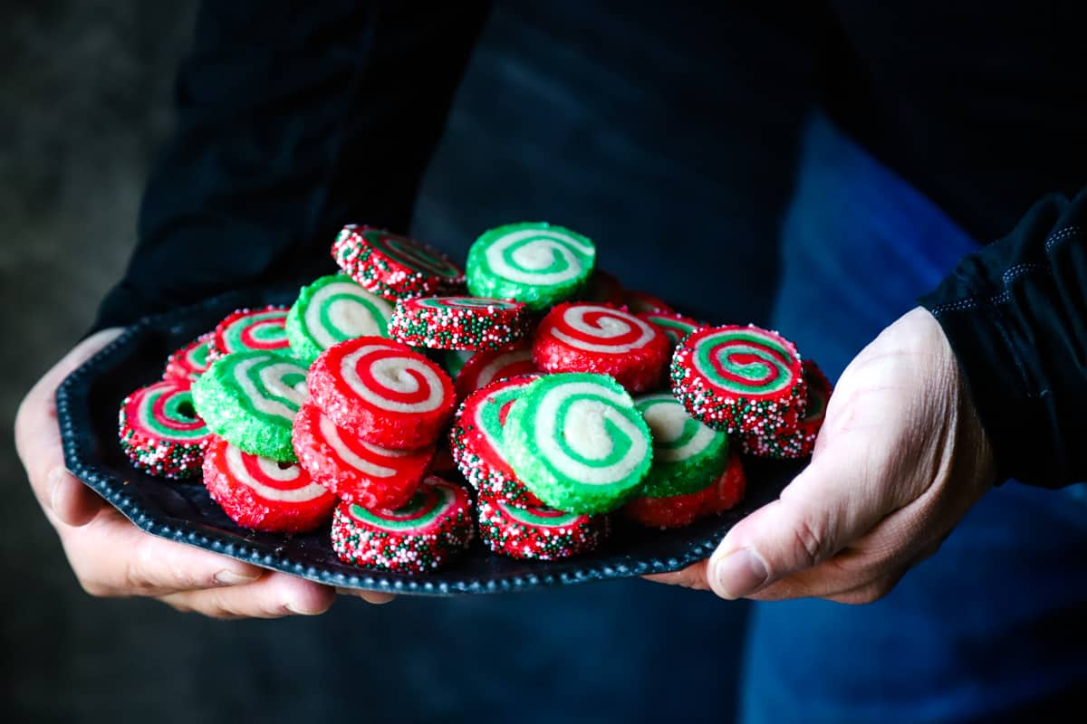 Hand holding a tray of red and green cookies. 