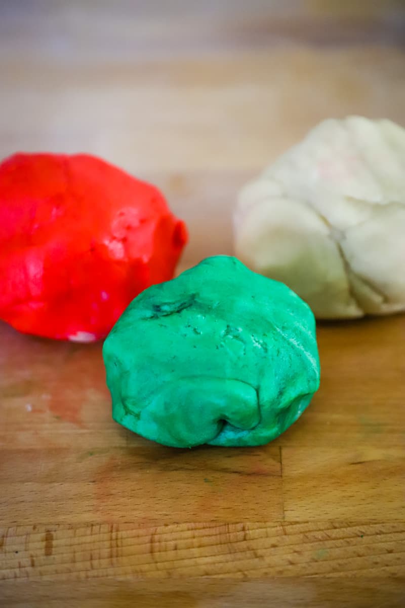 Balls of white, red, and green cookie dough on wood board. 