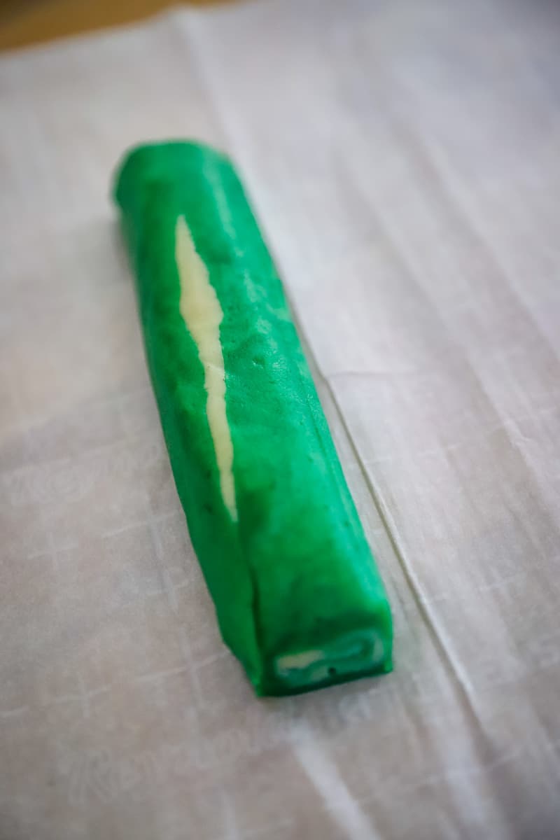 Rolled green and white dough rolled into a log on a piece of parchment paper. 