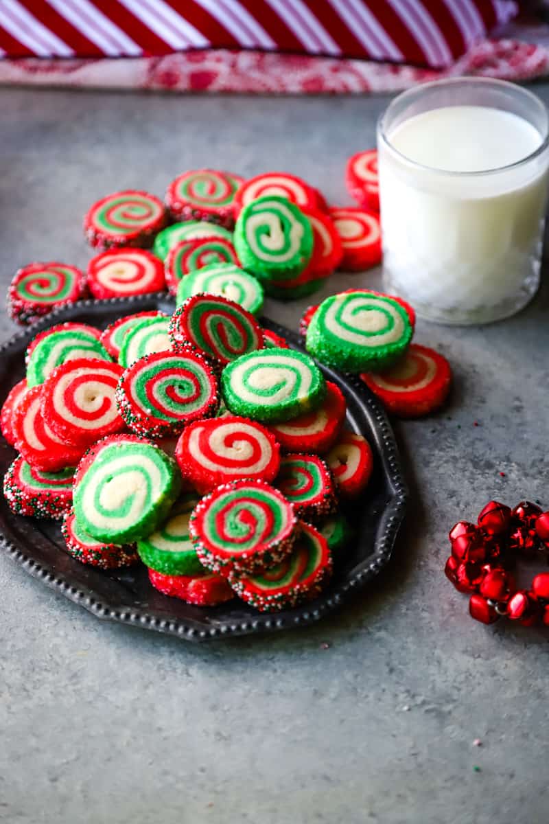 Tray of red and green pinwheel cookies and glass of milk. 
