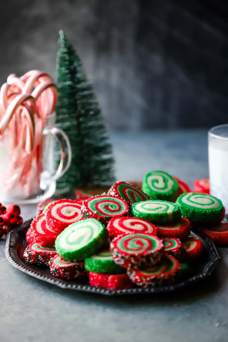 Tray of red and green cookies with candy canes and tree in background. 