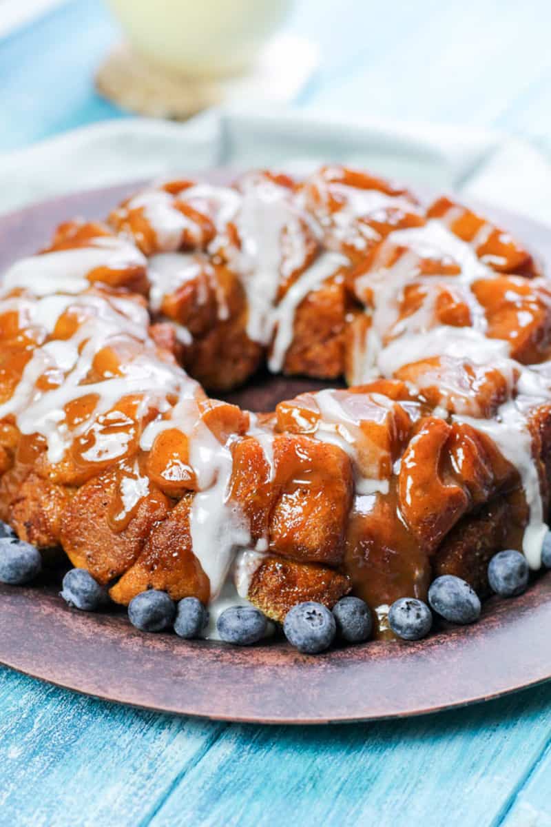 Monkey bread on a wood plate with blueberries on a bright blue backdrop.